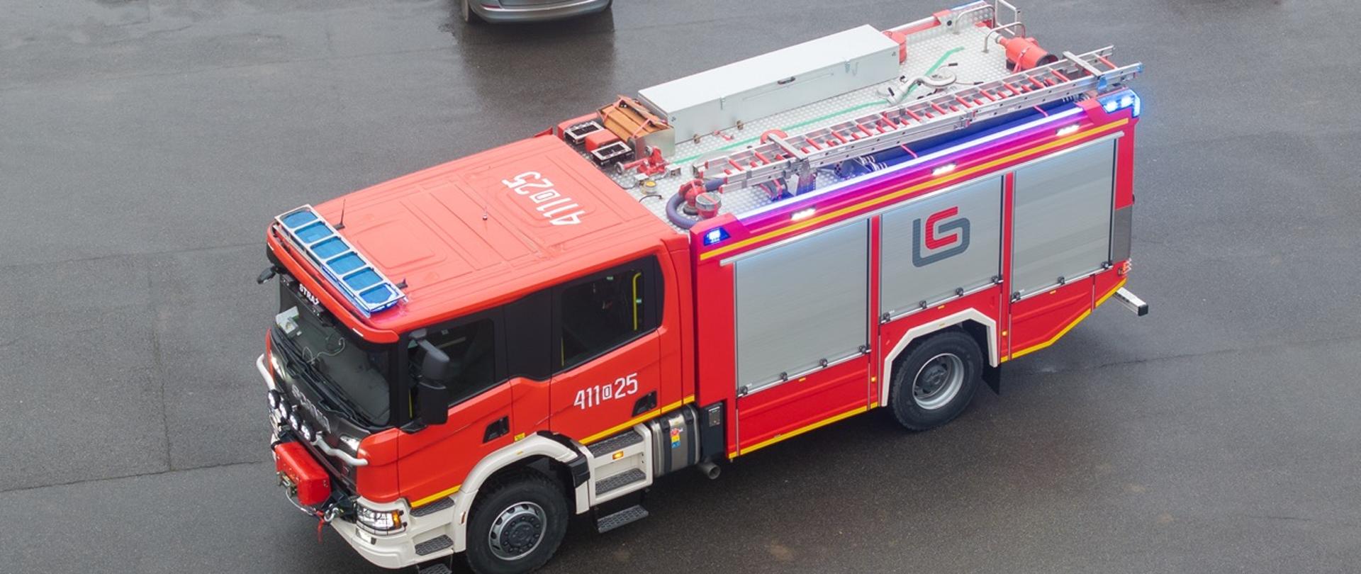 Widok z góry na ciężki samochód ratowniczo‑gaśniczy KP PSP w Głubczycach. Pojazd stoi na placu wewnętrznym komendy.