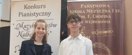 Zdjęcie kolorowe. Dwoje nastolatków stojących obok siebie między dwoma wysokimi, pionowymi banerami reklamowymi. Dziewczyna po lewej stronie ubrana w czarny, błyszczący strój i ciemną marynarkę, uśmiecha się. Chłopak po prawej stronie w białej koszuli z długim rękawem, granatowych jeansach i okularach na nosie, stoi prosto. Banery z napisami "Konkurs Pianistyczny 'Muzyka Krajów Nadbałtyckich'" i "PAŃSTWOWA SZKOŁA MUZYCZNA I ST. IM. F. CHOPINA W WEJHEROWIE" stanowią tło.