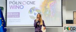 Kobieta w fioletowym garniturze przemawia do mikrofonu na tle ekranu z napisem: Północne Wino". 