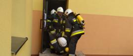 Ewakuacja osoby poszkodowanej (ratownika) przez trzech ratowników. Działania prowadzone są przy wyjściu z budynku.