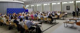 The photo shows a conference room filled with participants. On the right, Deputy Minister Jan Szyszko can be seen standing on stage