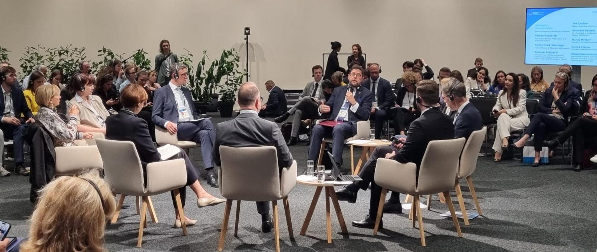 W dużej sali z szarymi ścianami na swobodnie porozstawianych krzesłach siedzą ludzie, pośrodku wiceminister Szeptycki mówi do trzymanego w ręku mikrofonu.