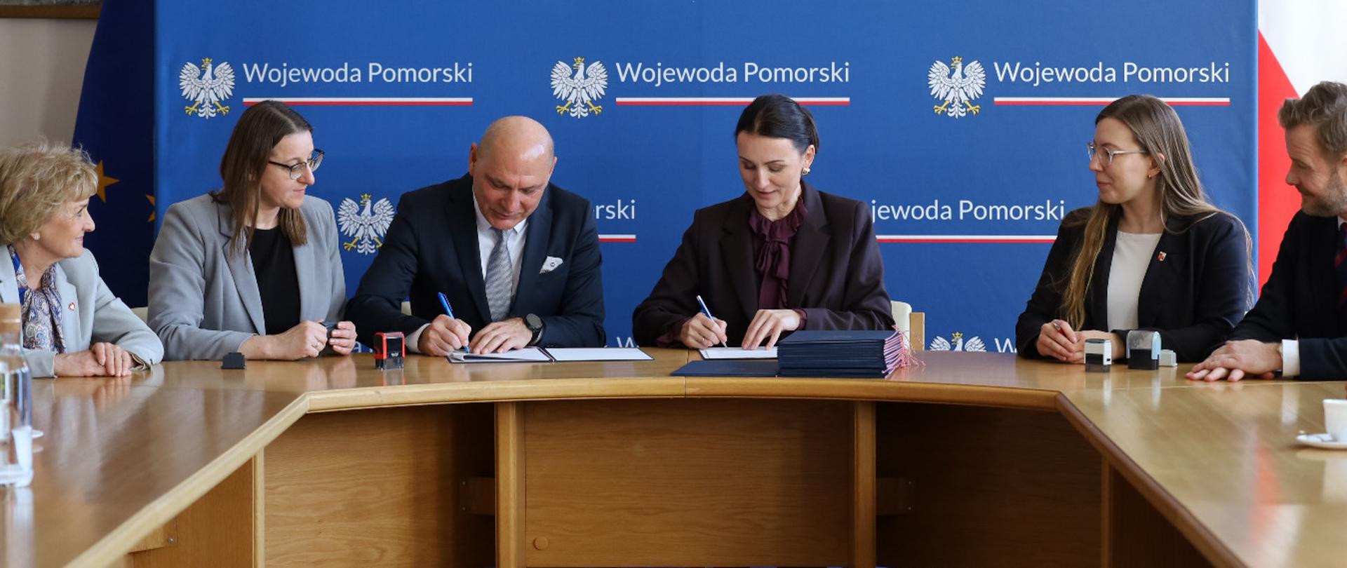 kilka osób siedzi przy stole i podpisuje dokumenty