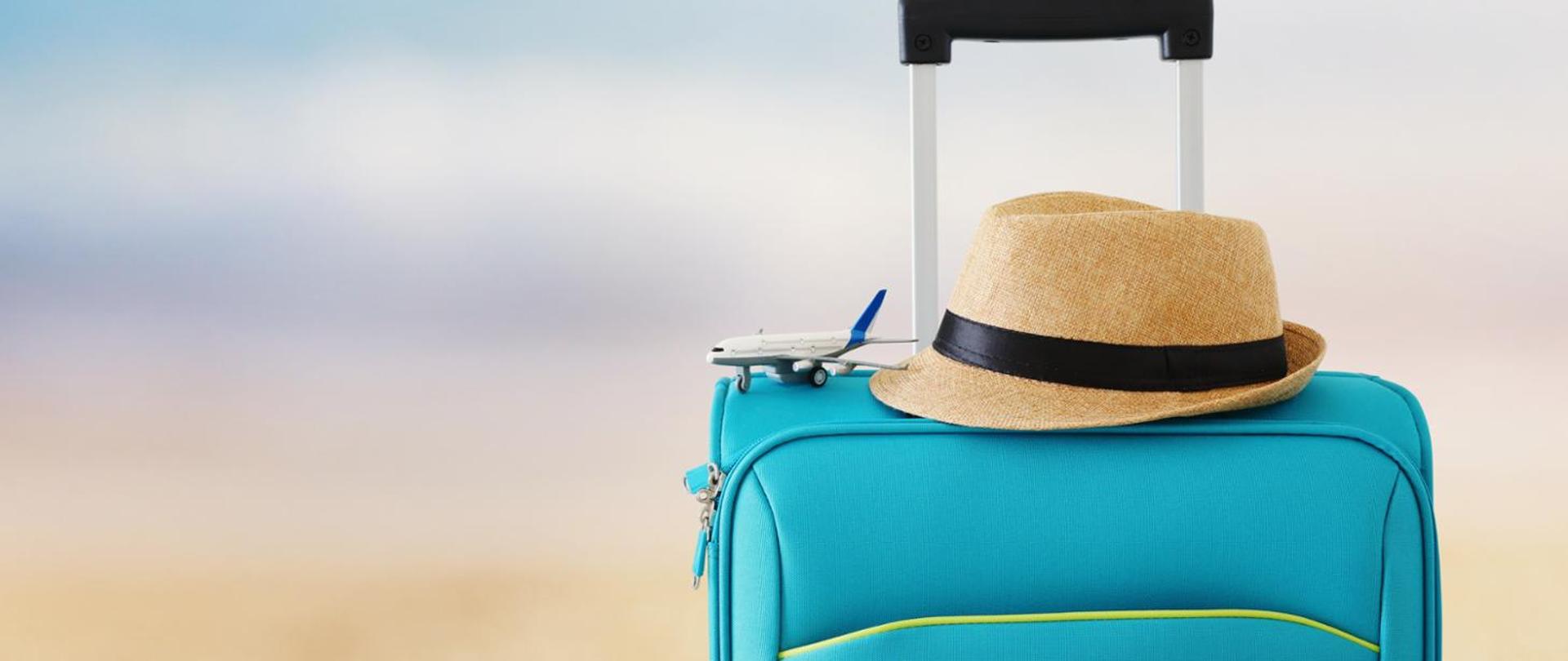 na zdjęciu widnieje torba podróżna, na niej jasny kapelusz i model samolotu pasażerskiego