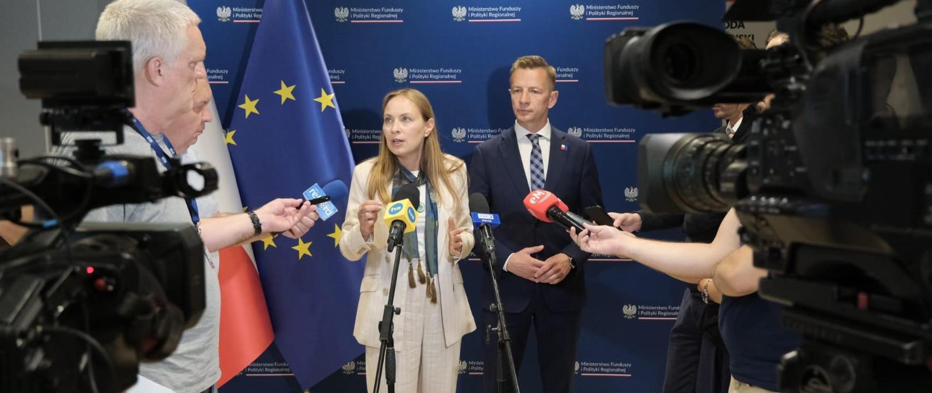 Dwie osoby stoją obok siebie przed kamerami. Pierwsza od lewej stoi minister Katarzyna Pełczyńska-Nałęcz.