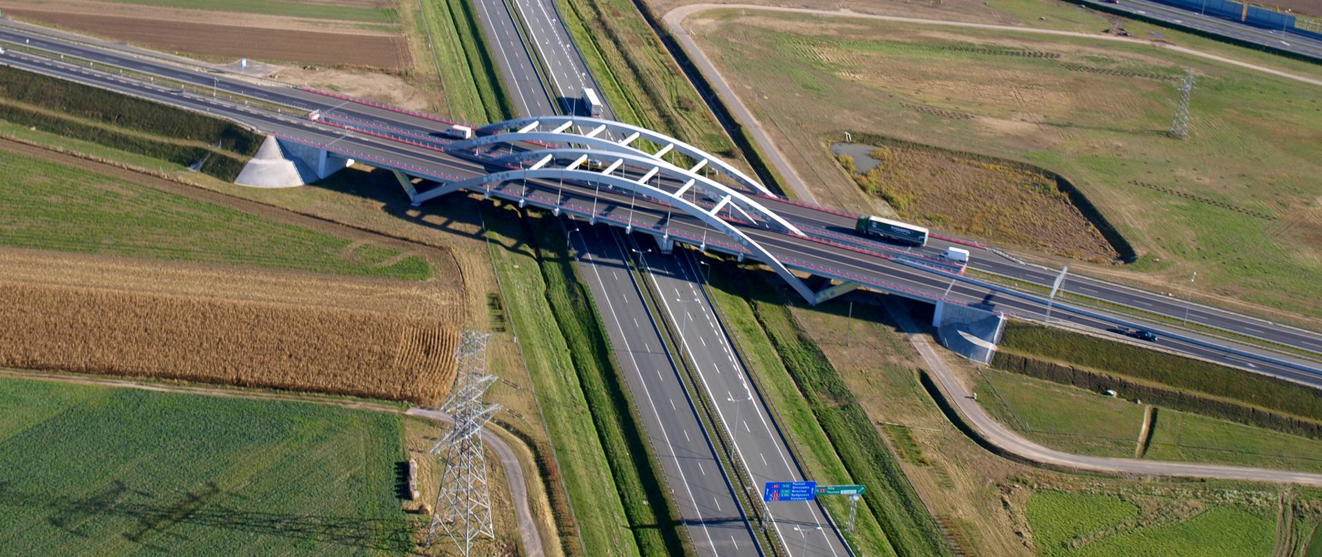 Widok z powietrza na węzeł Poznań Zachód, skrzyżowanie A2 z S5 i S11. Na pierwszym planie dwujezdniowa autostrada A2 i biegnące nad nią wiadukty dwujezdniowej drogi ekspresowej S5 i S11 oraz węzeł drogowy.