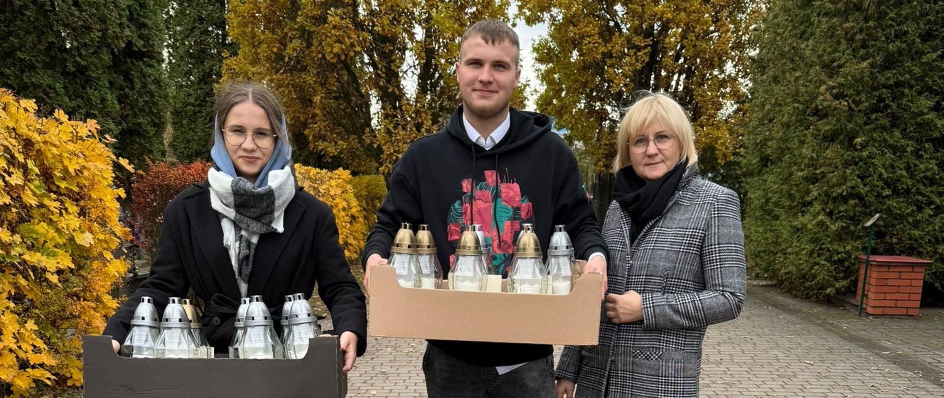 Uczniowie z opiekunką niosą przygotowane znicze od społeczności ZS CKR