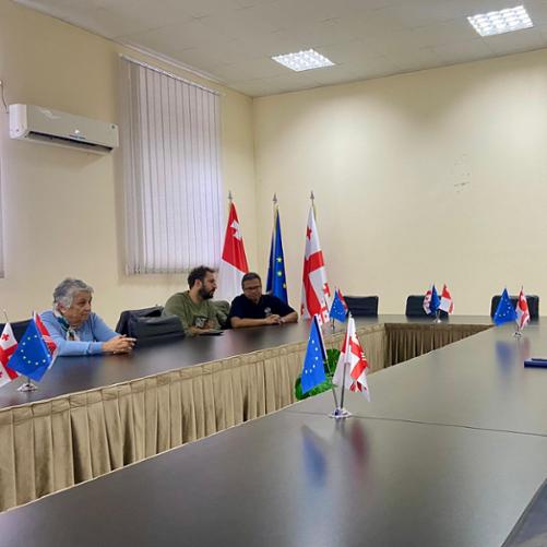 Przy stole z flagami Unii Europejskiej i Gruzji siedzą ludzie 