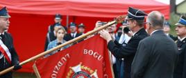 Druh OSP trzymający pochylony sztandar w stonę prezesa związku ochotniczych straży pożarnych, który dokonuje jego odznaczenia