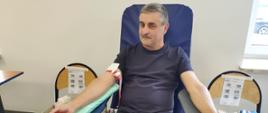 Na zajęciu widoczny mężczyzna siedzący na fotelu na sali oddający krew podczas akcji zbiórki krwi zorganizowanej przez Kluby Honorowych Dawców Krwi Polskiego Czerwonego Krzyża przy Komendzie Powiatowej Państwowej Straży Pożarnej w Gorlicach i Klub Honorowych Dawców Krwi Polskiego Czerwonego Krzyża Moszczenica