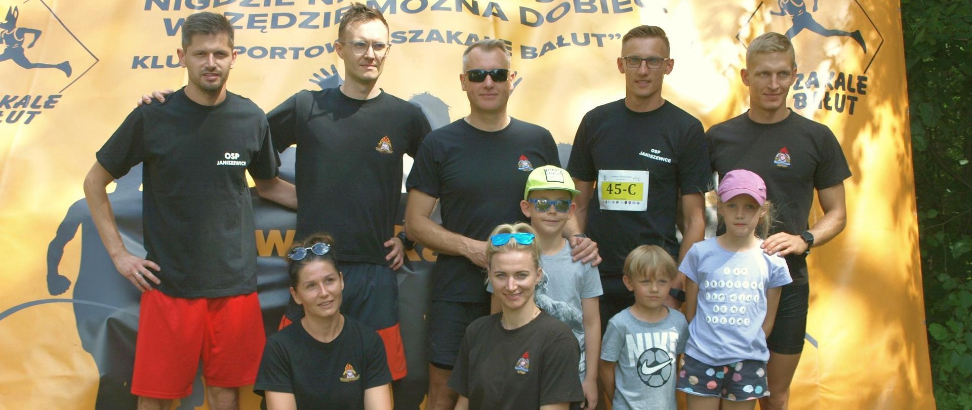 siedmioro strażaków w strojach sportowych oraz troje dzieci pozują do zdjęcia przy banerze reklamowym