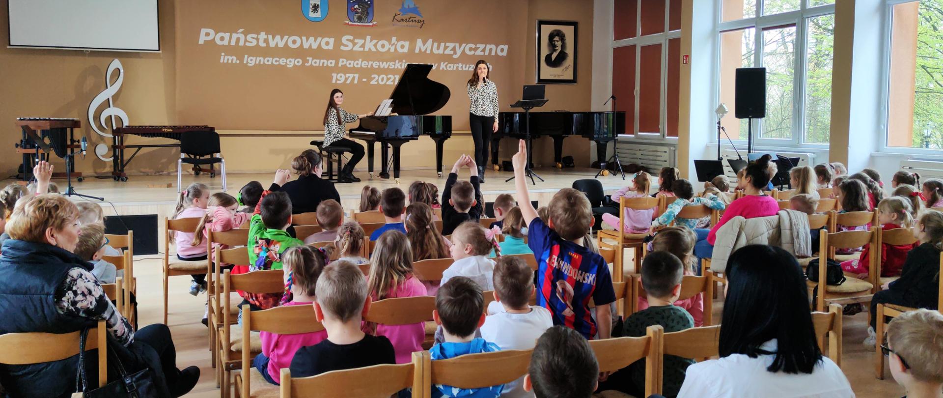 na widowni grupa przedszkolaków, na scenie osoby prowadzące spotkanie przy fortepianie