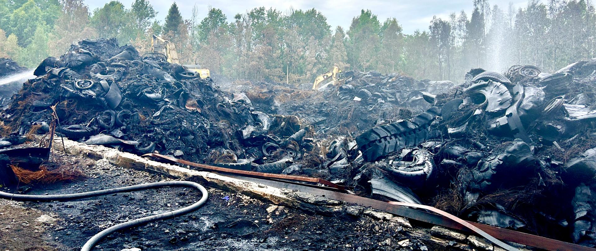widoczne pryzmy spalonych opon i materiałów gumowych, w tle prądy wody i rozwinięte węże gaśnicze