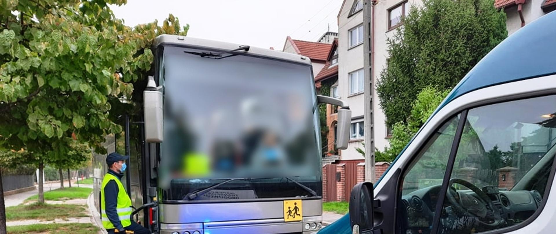 Kontrola drogowa ITD. Inspektor trzymający alkomat w dłoni stoi przed wejściem do autobusu. Przed autobusem stoi radiowóz ITD.