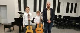 Nauczyciel z dwoma chłopcami stoi na scenie. Chłopcy trzymają gitary.