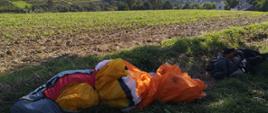 Zdjęcie przedstawia paralotnię i odzież leżącą na ziemi. W tle krajobraz Beskidu Wyspowego.
