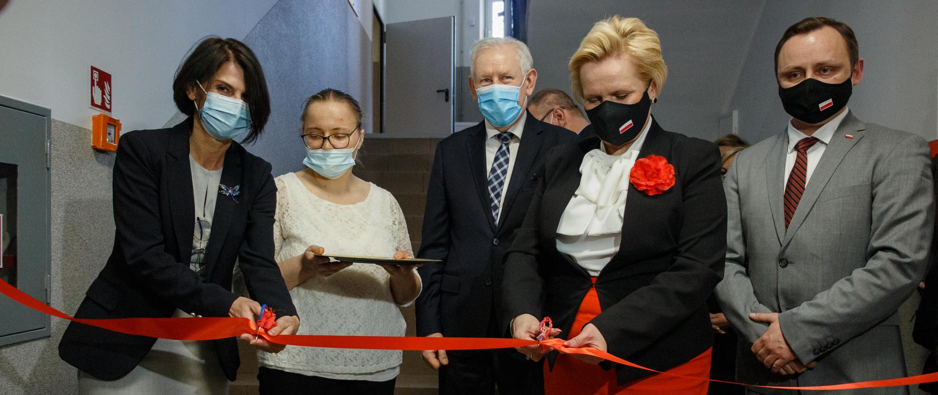 Na zdjęciu 4 osoby stojące w szeregu, przecinające wstęgę biało-czerwoną. Na pierwszym planie, tj. w środku kadru wicewojewoda, ubrana w czarny żakiet i czerwoną spódnicę. Obok dwie kobiety, z czego jedna także przecina wstęgę a druga - oddalona nieco od kadru - trzyma w dłoniach tacę.