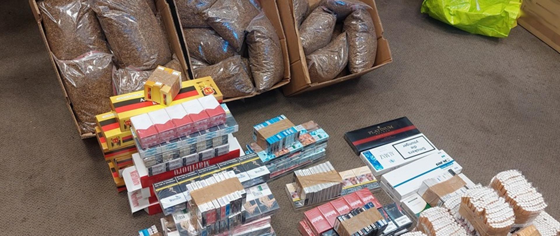Papierosy i tytoń ułożone na podłodze pomieszczenia.
