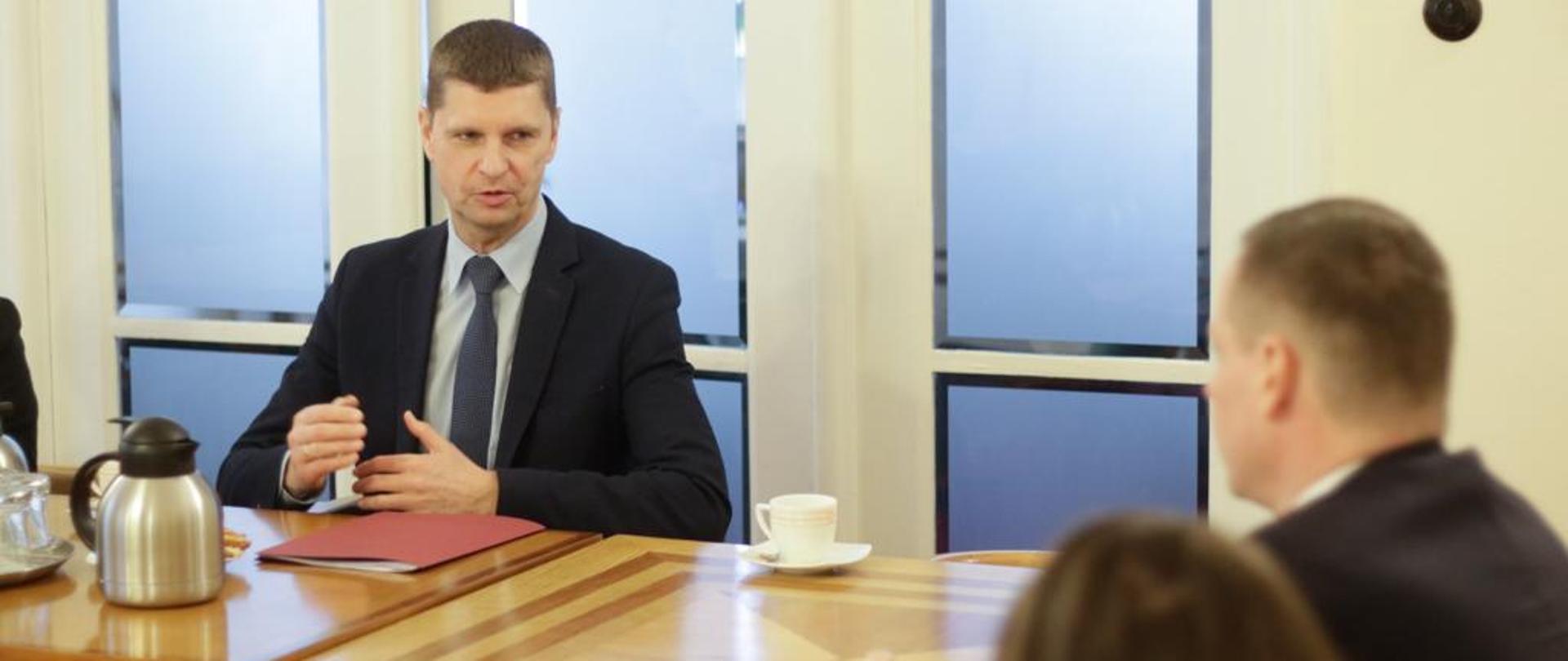 Wiceminister Dariusz Piontkowski siedzi przy stole i rozmawia z ambasadorem Andrejem Drobą, który siedzi po drugiej stronie stołu.