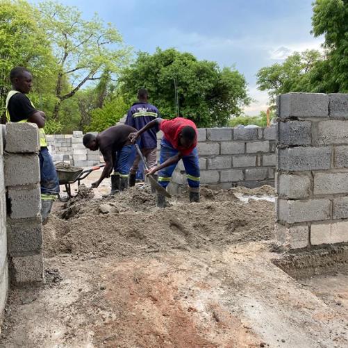 Grupa robotników pracuje na terenie budowy, przerzucając materiał budowlany przy użyciu łopat