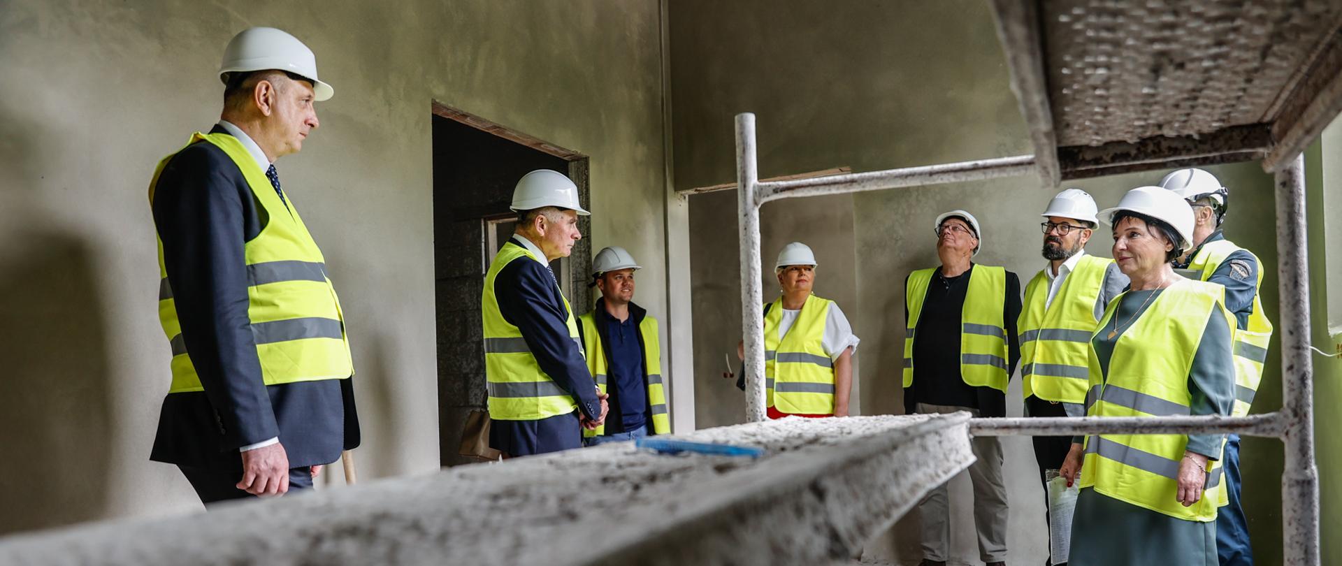 Kobiety i mężczyźni w kaskach i kamizelkach na budowie. 