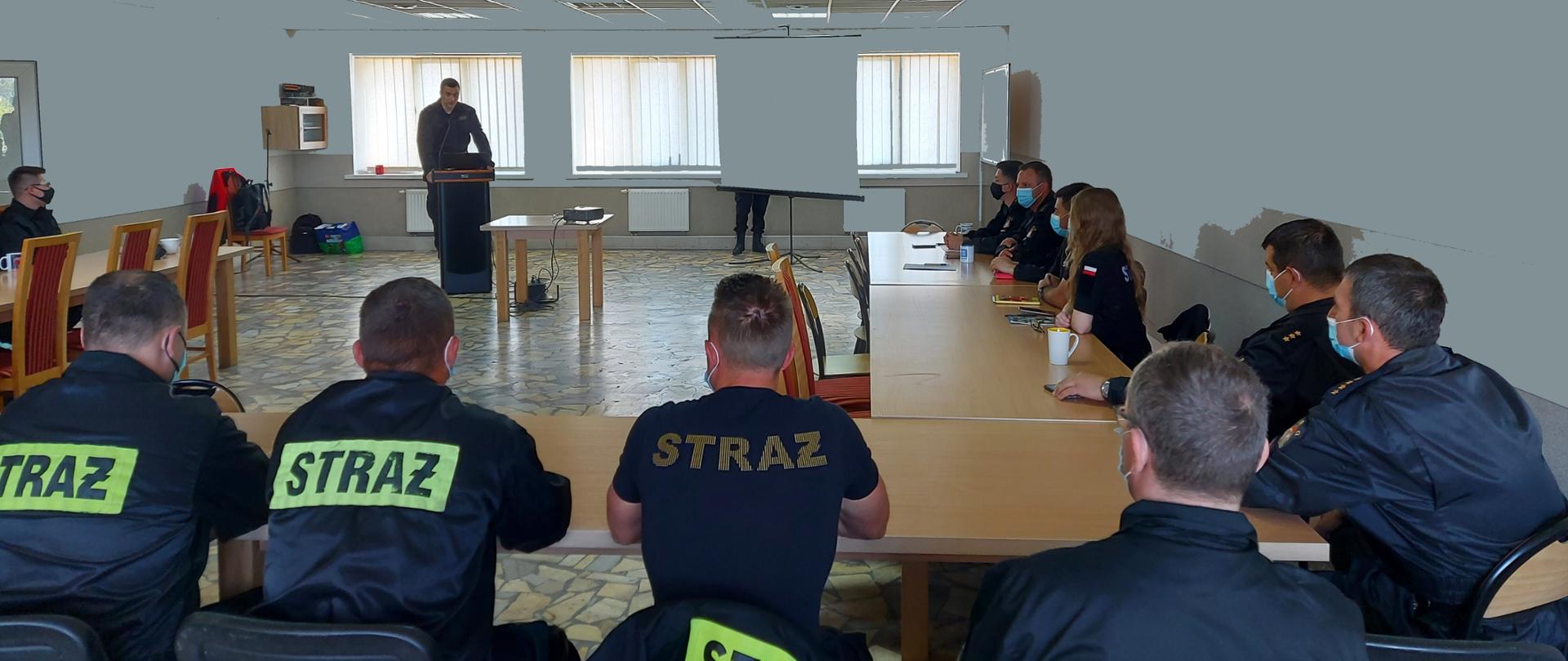 Na zdjęciu wiać siedzących uczestników szkolenia, na drugim planie w oddaleniu za mównicą stoi prowadzący zajęcia. 
