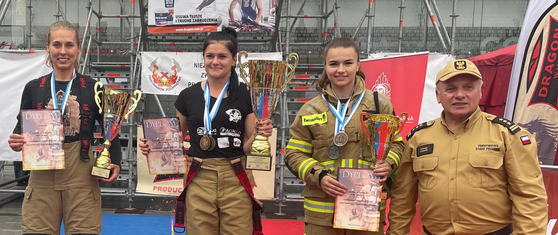 Na zdjęciu podium kategorii indywidualnej kobiet stoją funkcjonariuszki z dyplomami i medalami obok nich krakowski funkcjonariusz PSP