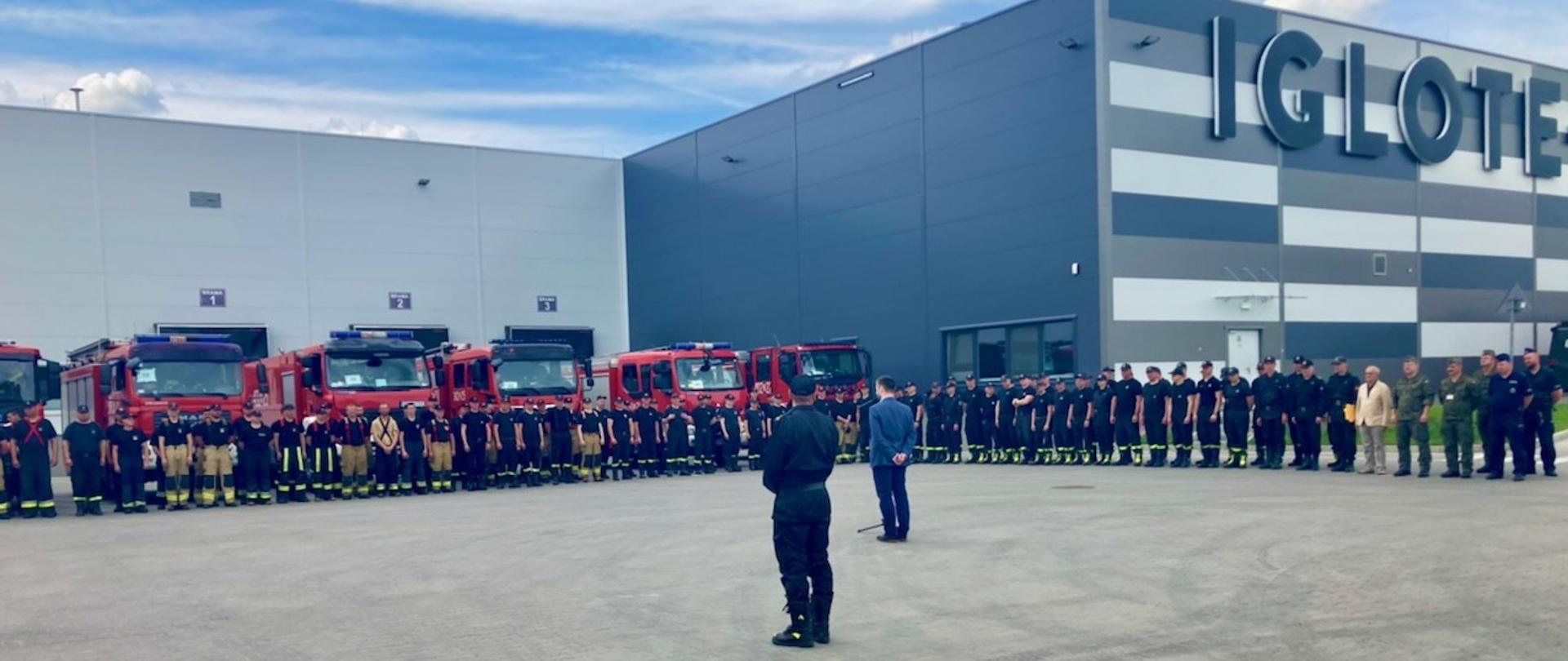 Pod budynkiem firmy IGLOTEX ustawiono pojazdy które brały udział w ćwiczeniach, a przed nimi ćwiczących funkcjonariuszy