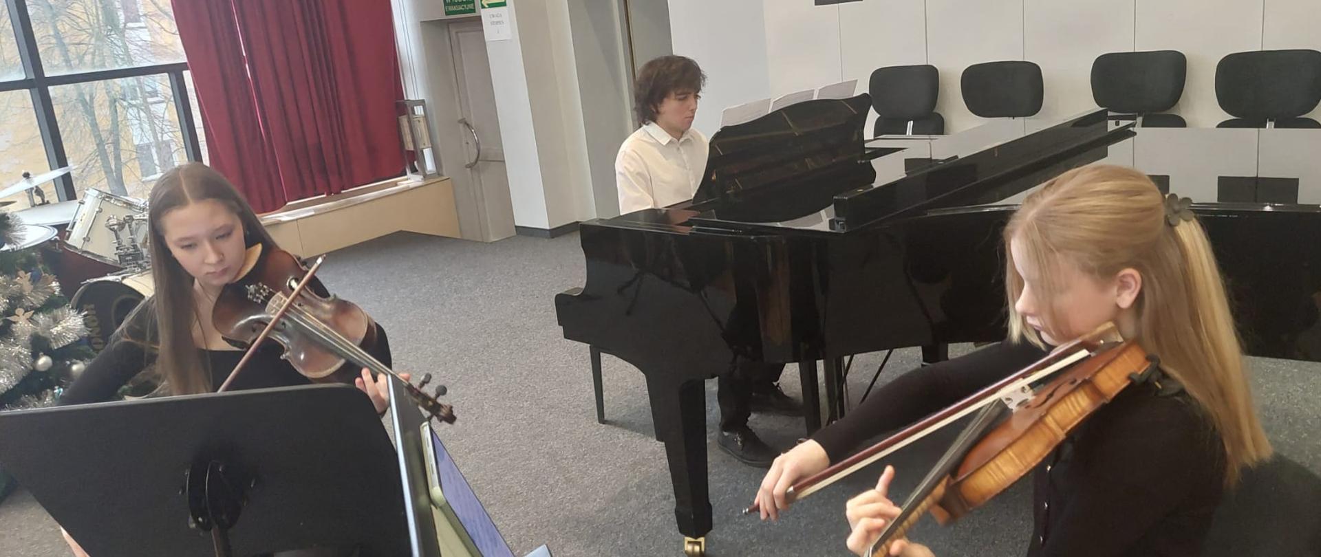 Dwie dziewczyny grają na skrzypcach, chłopak gra na fortepianie.
