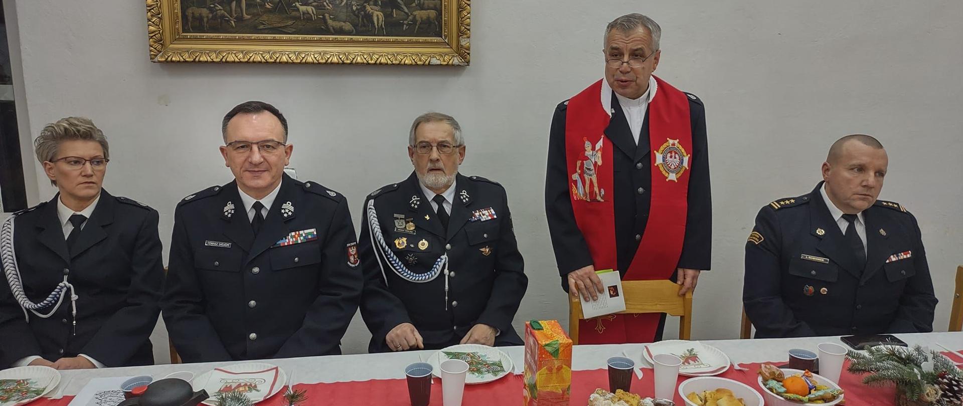 Przy świątecznym stole siedzą strażacy w mundurach.