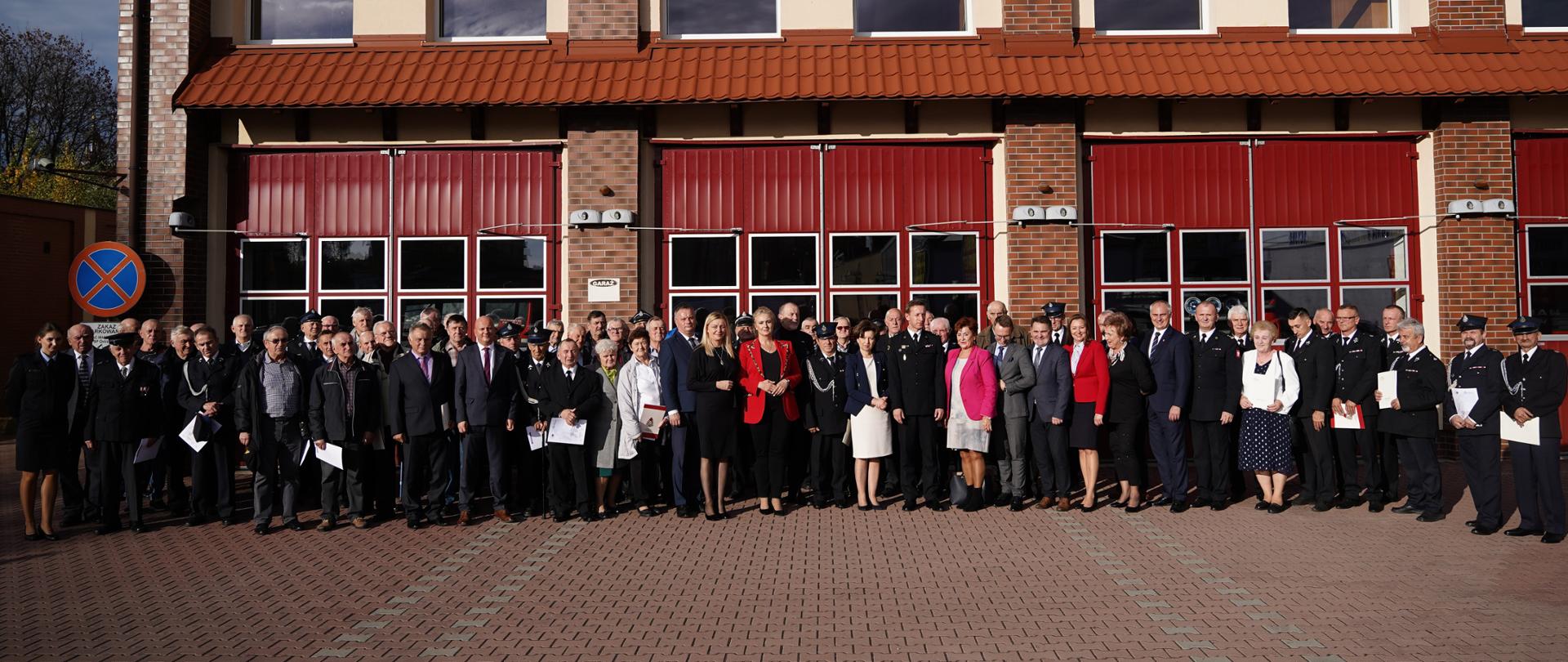 Zdjęcie grupowe uczestników wydarzenia. W tle budynek strażnicy.