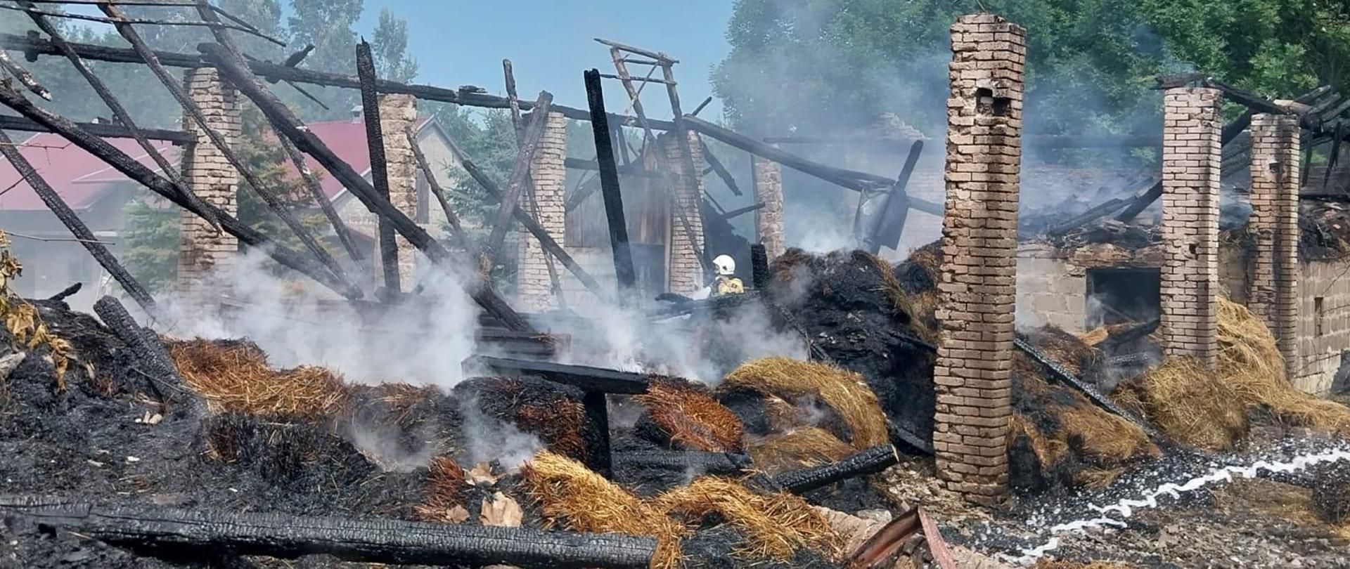 Zawalona konstrukcja drewniana, stoją murowane filary, na dole spalona słoma