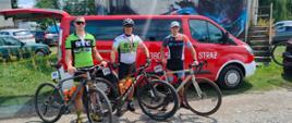Trzech sportowców stoi przy swoich rowerach na tle samochodu strażackiego.