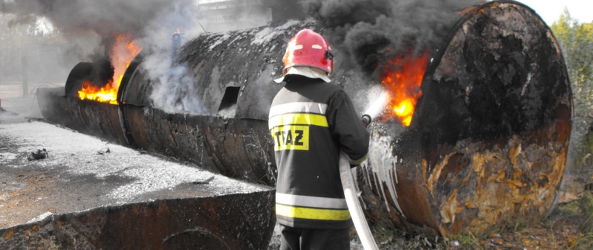 Zdjęcie przedstawia strażaka podającego pianę na zbiornik