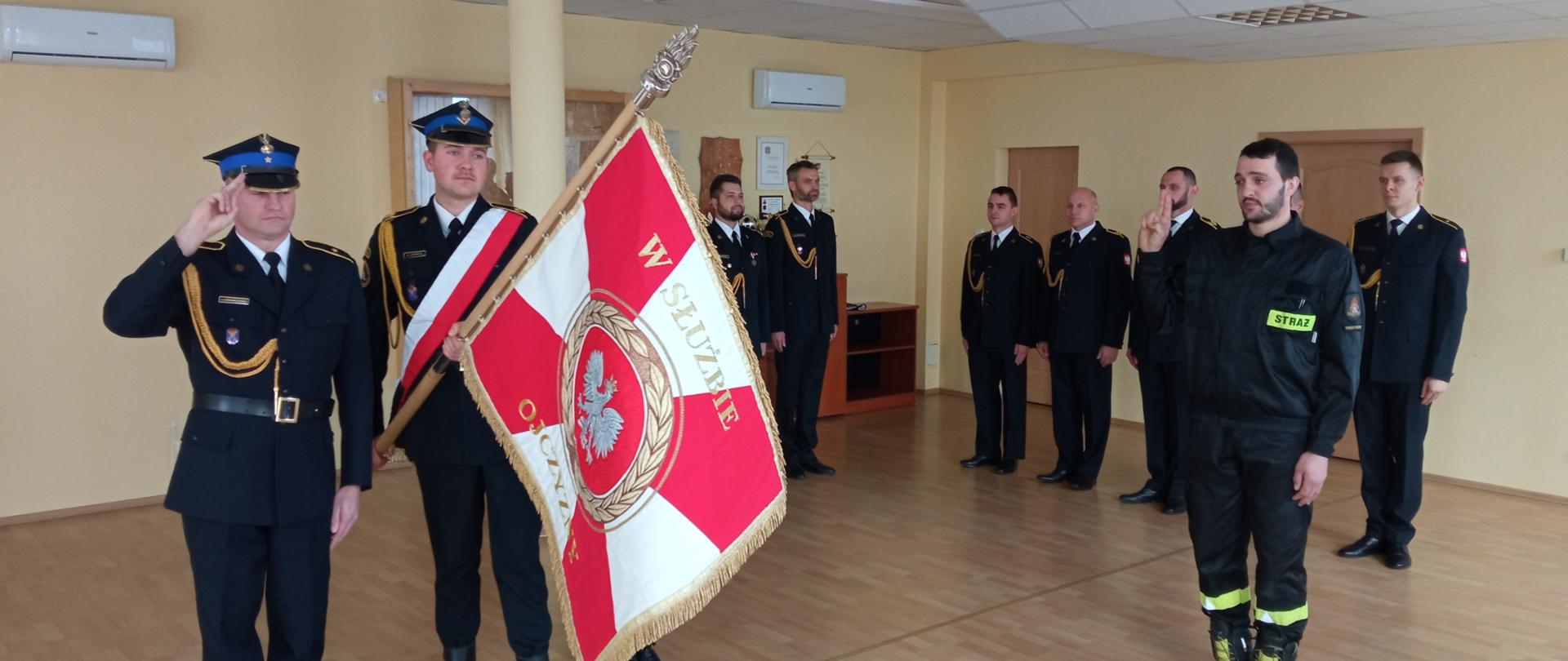 Fotografia przedstawia moment ślubowania na sztandar nowego funkcjonariusza Państwowej Straży Pożarnej.