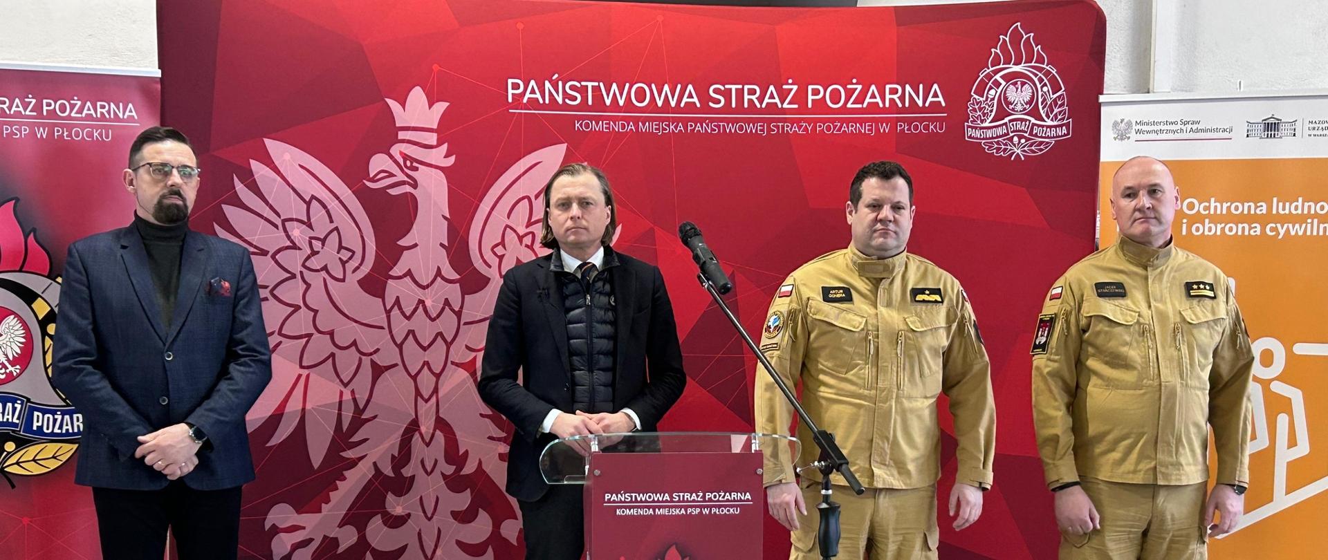 Konferencja prasowa w siedzibie PSP – przedstawiciele Państwowej Straży Pożarnej i administracji publicznej stoją przy mównicy z logo PSP podczas wystąpienia.