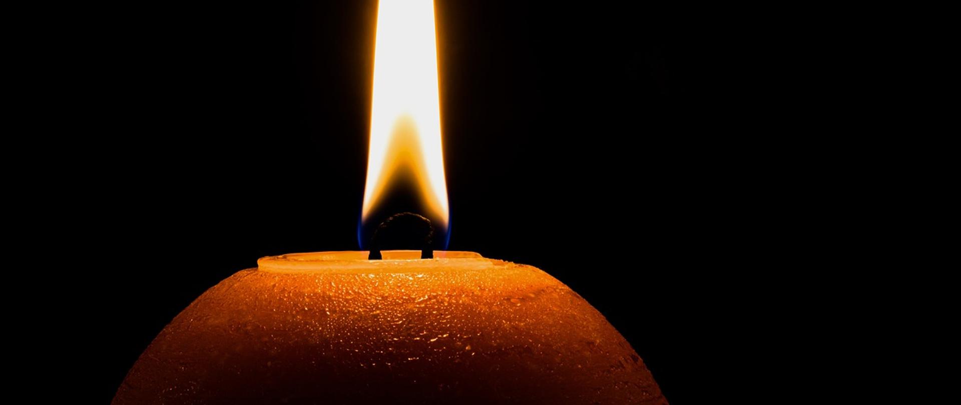 Zdjęcie przedstawia płonącą świece na czarnym tle