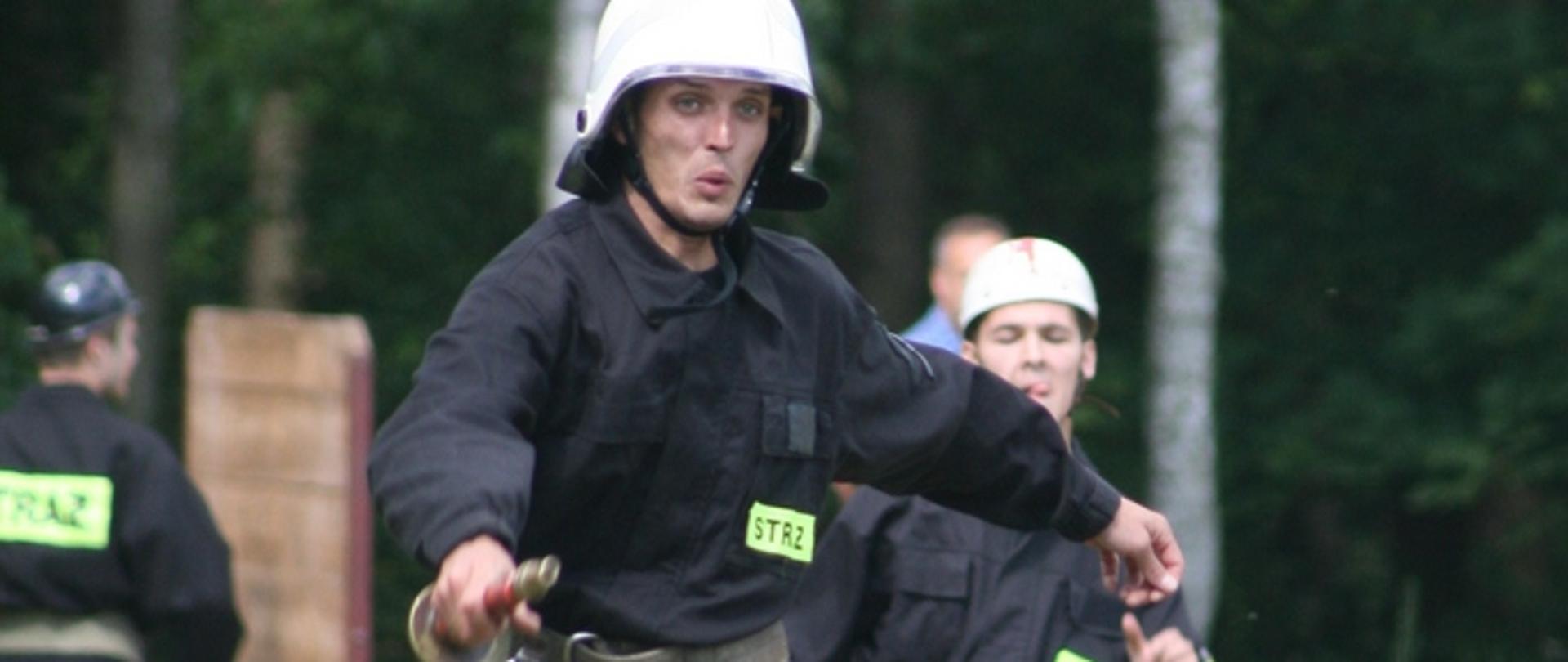 Zdjęcie przedstawia strażaka przeskakującego przez płotek