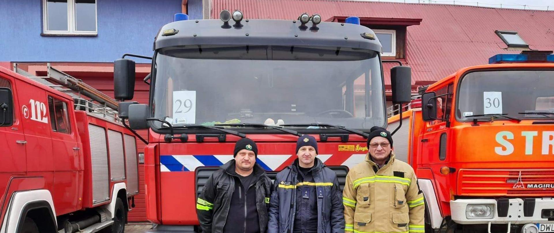 Obraz przedstawia strażaków OSP Budziszów Wielki ze strażakami z Ukrainy. W tle przekazywany samochód pożarniczy. 