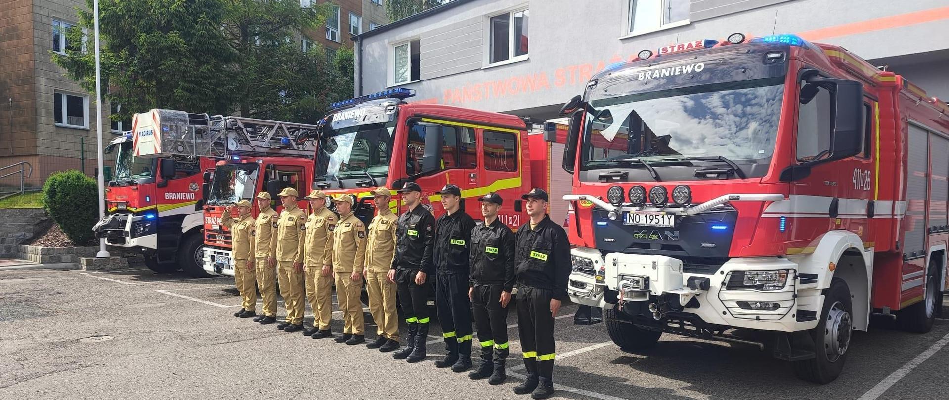 Na zdjęciu grupa strażaków ustawionych w szeregu na tle samochodów strażackich.