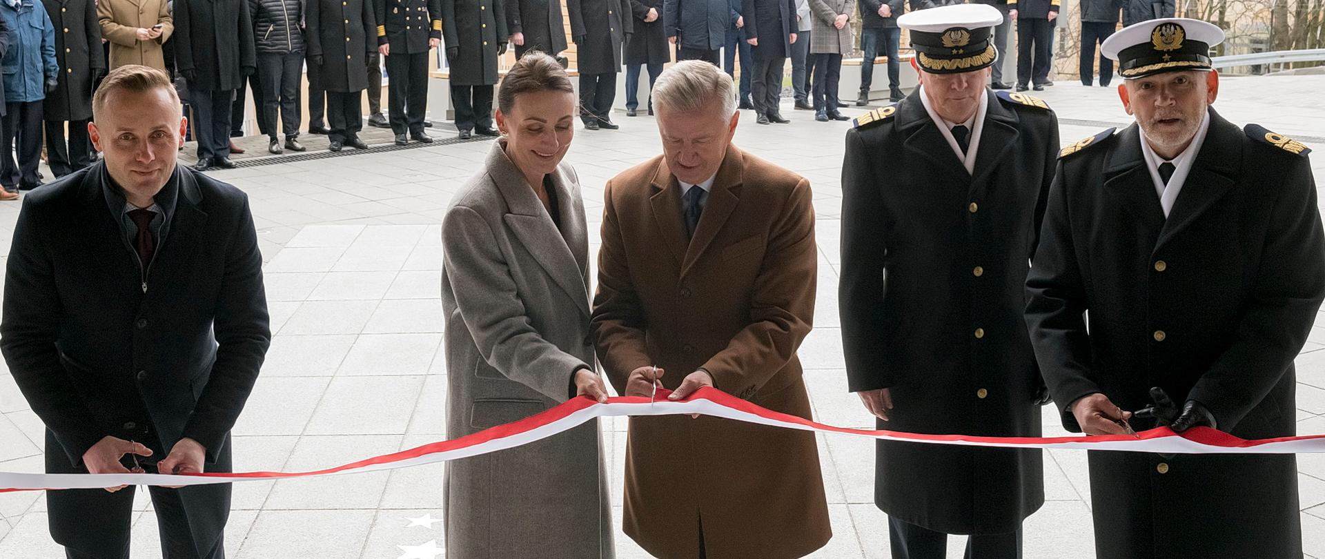 kilka osób, w tym kobieta i marynarze przecinają wstęgę przed budynkiem