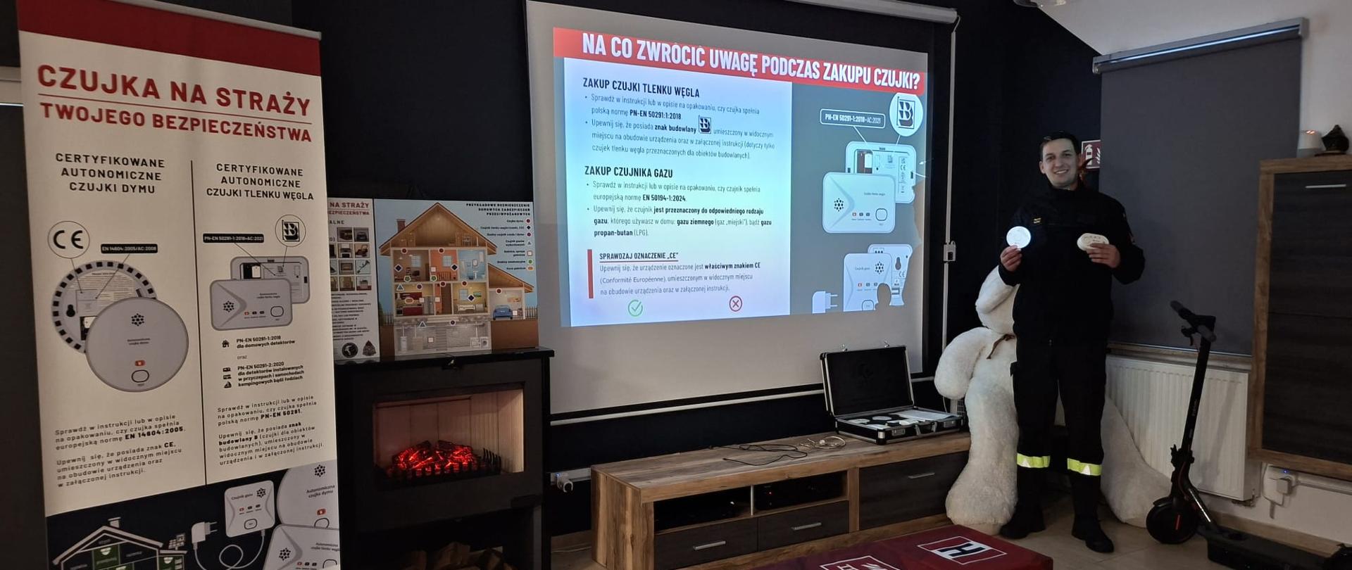 Na zdjęciu strażak, który prezentuje czujkę dymu i czadu w ogniku