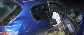 Kolizja samochodu osobowego. Na poboczu drogi polnej stoi samochód osobowy uczestniczący w zdarzeniu. Widok z zewnątrz od strony prawej (pasażera). Otwarte są drzwi auta. Na karoserii widoczne są wgniecenia, a także uszkodzona jest tylna lampa. 