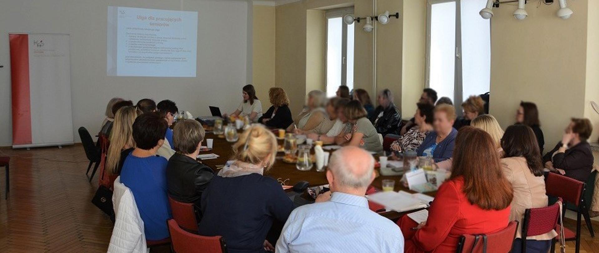 Uczestnicy szkolenia siedzą w sali. Na ekranie wyświetlana jest prezentacja.