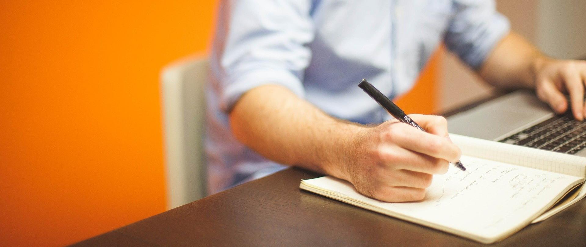 mężczyzna siedzący przy biurku robi notatki.