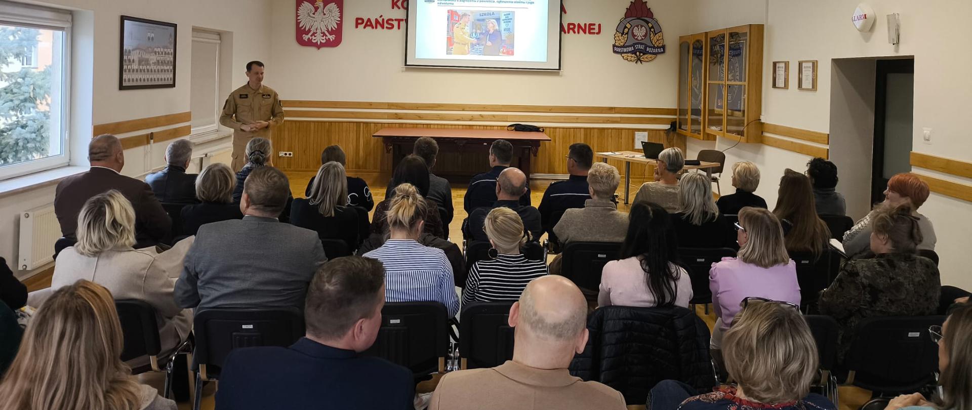 Zdjęcie przedstawia funkcjonariuszy Komendy Powiatowej Państwowej Straży Pożarnej w Zambrowie oraz Komendy Powiatowej Policji w Zambrowie w ubraniach służbowych podczas przedstawiania prezentacji dla dyrektorów szkół.