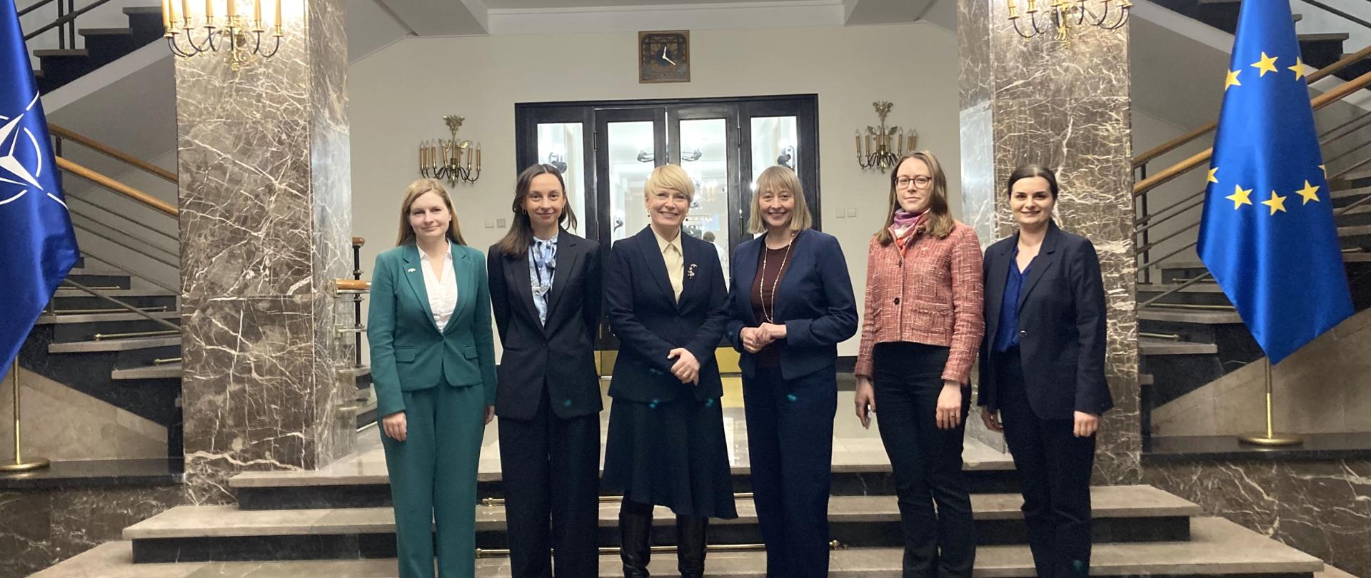 Sześć kobiet pozuje do zdjęcia w formalnej sytuacji z flagą Unii Europejskiej