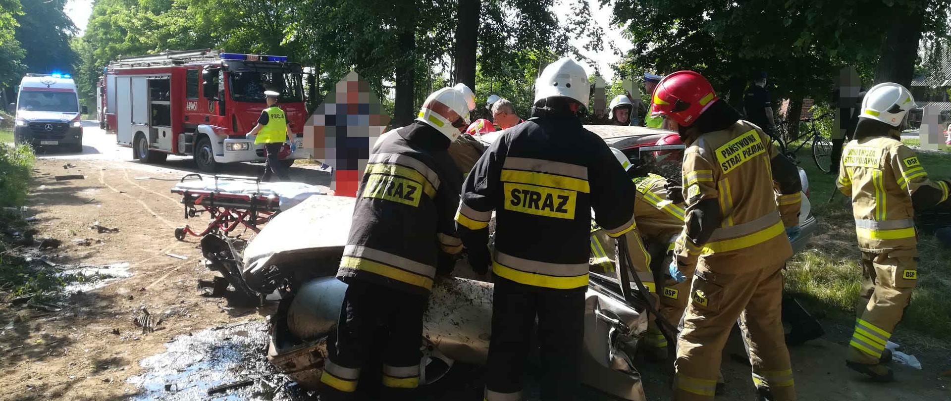 Zdjęcie przedstawia rozbity samochód i strażaków wykonujących dostęp do uwięzionej osoby przy pomocy narzędzi hydraulicznych.