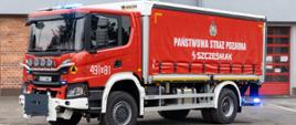 Czerwony ciężki samochód kwatermistrzowski Państwowej Straży Pożarnej stoi na placu przed strażnicą. Pojazd ma zabudowę kontenerową z plandeką, oznaczenia „PAŃSTWOWA STRAŻ POŻARNA” oraz numer operacyjny 491[O]81. Widoczne są przednie światła ostrzegawcze i wyposażenie typowe dla pojazdów logistycznych.