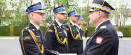 Na placu stoją strażacy którym wręczane są awanse na wyższy stopień.